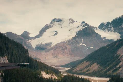 Scenic mountain range with snow-capped peaks, evergreen trees, and river Stock Photos