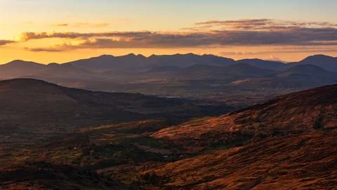 Scenic mountain range at sunset displays warm orange light Stock Photos