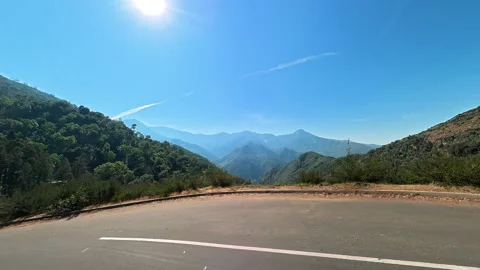 Scenic mountain road overlooking a deep green valley under clear blue sky 库存影片 343377785