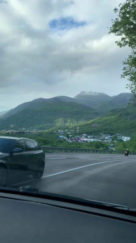 A scenic mountain road winding through lush green hills under a partly cloudy sk Stock Footage 296284720