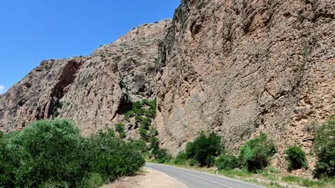 Scenic mountain road winds through rocky desert canyon with greenery along ed Video stock 339644758