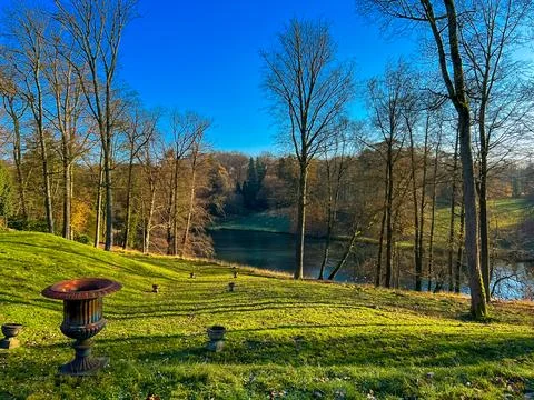 A scenic park view featuring leafless trees, a lake, and an old sculpture Stock Photos