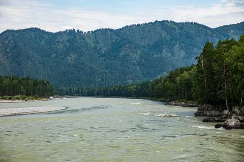 A scenic river flows gently, flanked by trees and mountains Stock Photos