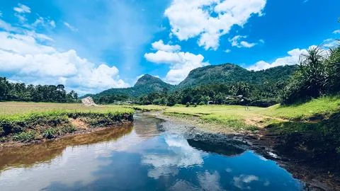 Scenic river stream reflecting blue sky and green hills in Kerala countryside Stock Photos