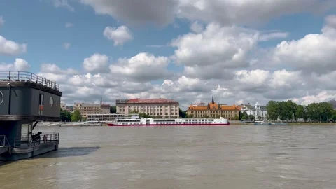 A scenic river view with a docked black boat in the foreground, cruise ship Stock-Footage 301279259