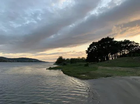 Scenic river view with trees and cloudy sky at sunset Stock Photos