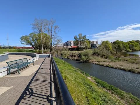 Scenic riverfront landscape with a passing train, park bench, trees 库存照片