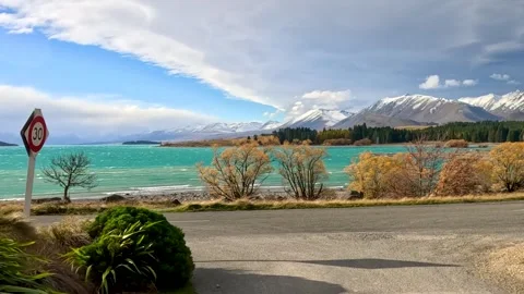 Scenic Road Approaching Turquoise Alpine Lake and Snow Capped Mountains 库存影片 325689708