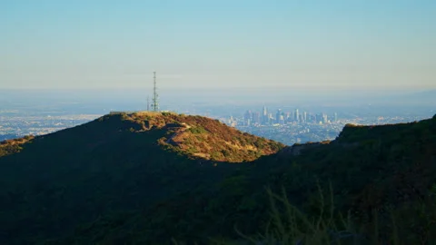 A scenic shot featuring the green mountain top in the foreground with the city Видео 282000711