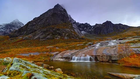 Scenic small waterfall flows over rocks into calm mountain pond with massive Stock Footage 343696692