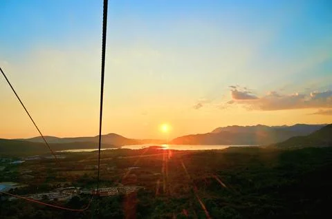 Scenic sunset landscape view with cable car cables over sea, mountains, and city Stock Photos