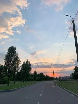 Scenic sunset over a quiet road with birds flying in the sky Stock Photos