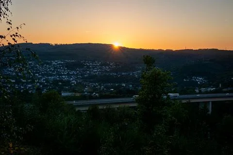 Scenic sunset view with sun rays over hills, city houses in valley and highway. Stock Photos