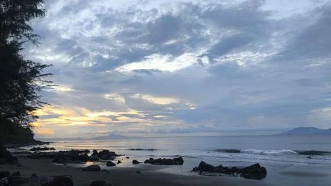 Scenic Tropical Beach at Sunset with Dramatic Cloudy Sky and Coastal Rocks Stock Photos