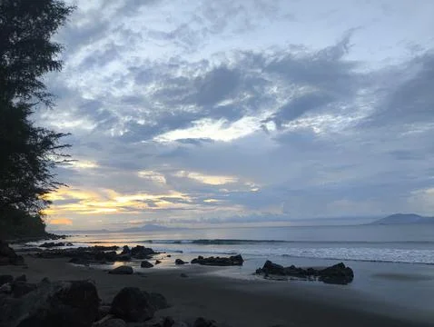 Scenic Tropical Beach at Sunset with Dramatic Cloudy Sky and Coastal Rocks Stock Photos
