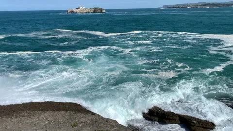 Scenic turquoise ocean waves rolling gently with a lighthouse in the background Stock Footage 314546453