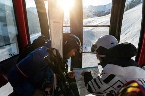 Scenic two skiers study trail map inside ski lift gondola at warm sunrise lig Фото