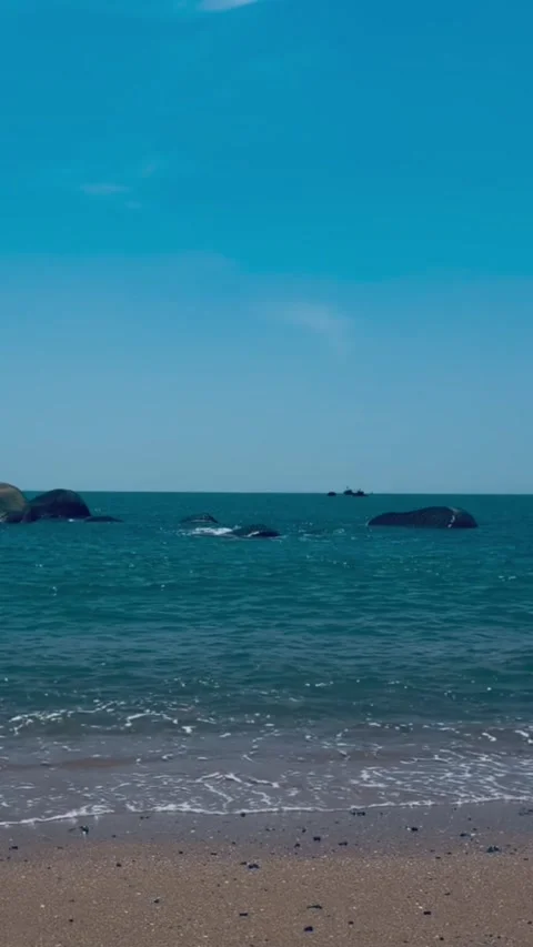 Scenic view of a calm ocean beach with large rocks scattered in the water under Vidéo 334163607