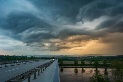 Scenic view of dark clouds loom above a bridge over a river, surrounded by trees 写真素材