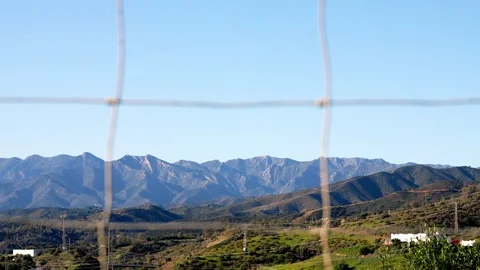 Scenic view of distant mountain range framed through a wire fence with lush Stock Footage 296588617