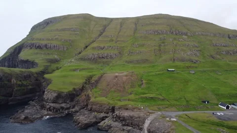 Scenic view flying over cliffs towards a football pitch and village, Suduroy Stock Footage 340168765