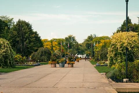 A scenic view of a garden path lined with trees and flower pots in the park Stock Photos