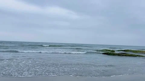 Scenic view of ocean waves crashing against mossy rocks on a cloudy day Vidéo 334084371