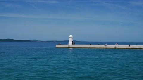 Scenic view over blue sea to the white lighthouse on Zadar Riva pier with Vídeo Stock 342352955