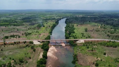 Scenic view of a river flowing through a lush green landscape with a bridge Stock Footage 318320290