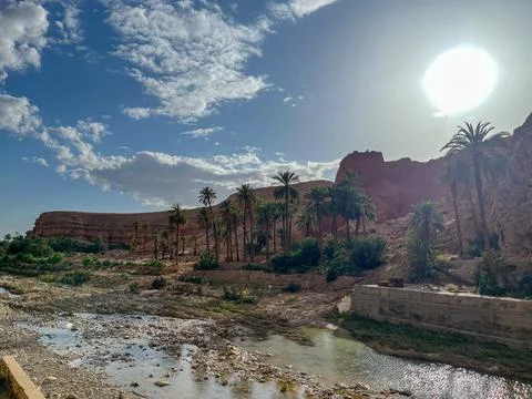 Scenic view of a river flowing through a palm tree oasis at the base of rocky Stock Photos