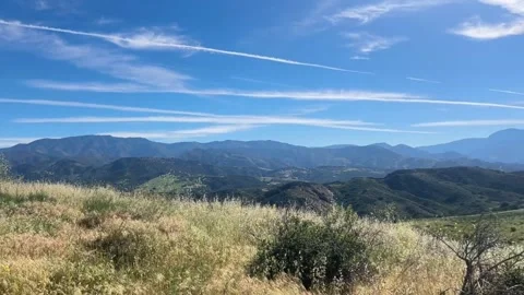 Scenic view of rolling hills and mountains under a bright blue sky with wispy Vidéo 334163640