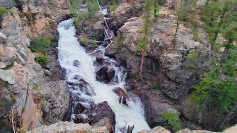 Scenic view of a rushing waterfall cutting through rocky cliffs and evergreen Stock Footage 334100021