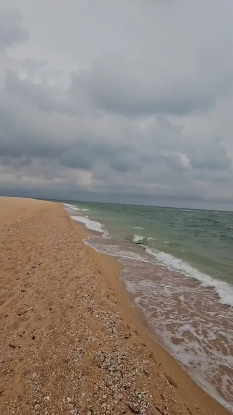 Scenic view of a sandy beach coastline with gentle waves under a cloudy sky Vidéo 334083975