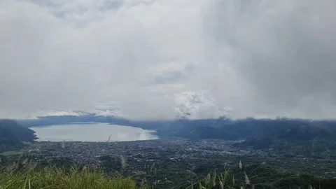 A scenic view of a town nestled between a lake and mountains, under a cloud.. Stock Footage 291380982
