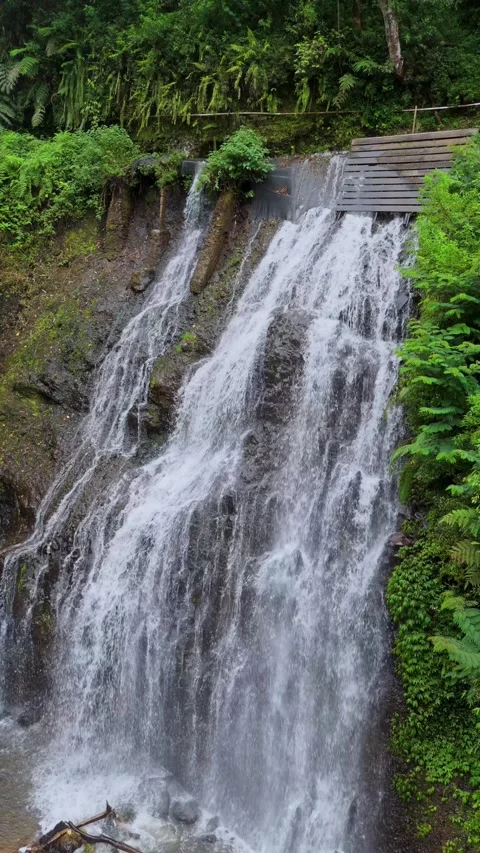 Scenic view of tropical waterfall cascading down rocky cliffs into hidden pool Stock Footage 332745136