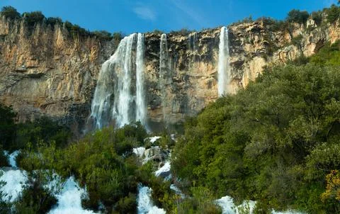 Scenic view of a waterfall flowing down a rocky cliff surrounded by a dense f Stock Photos