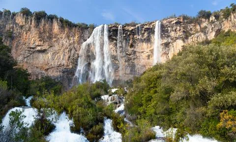Scenic view of a waterfall flowing down a rocky cliff surrounded by a dense f Stock Photos