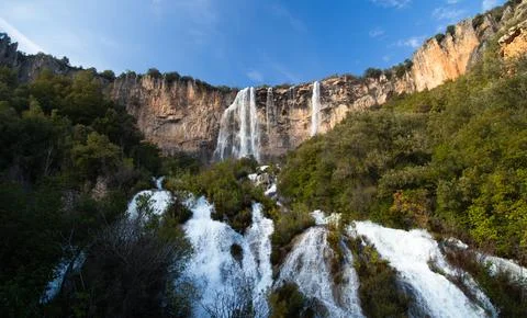 Scenic view of a waterfall flowing down a rocky cliff surrounded by a dense f Stock Photos