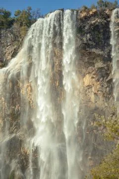 Scenic view of a waterfall flowing down a rocky cliff surrounded by a dense f Stock Photos
