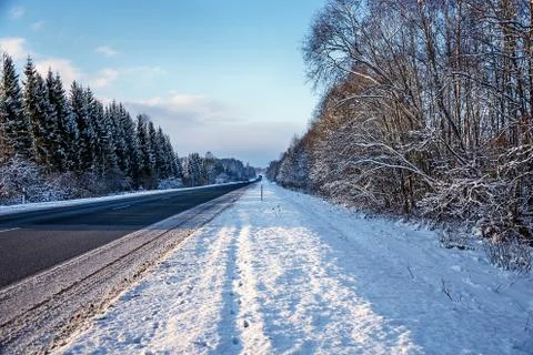 Scenic view of a winter empty road with snow, illuminated by the sun. Stock Photos