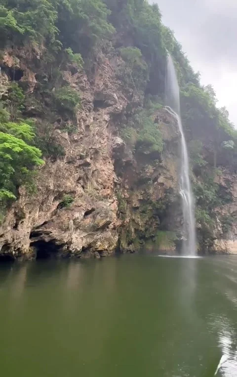 Scenic Waterfall Cascading Down Lush Green Cliffs Into Calm Reservoir Water Vidéo 333605137