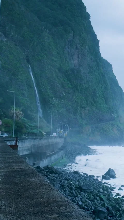 Scenic waterfall cascading over a cliff onto a coastal road in madeira Stock Footage 334440690