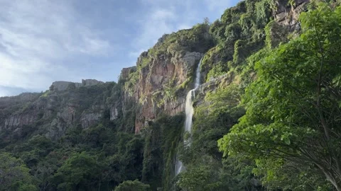Scenic waterfall cascading over a lush green cliff beneath a blue sky Stock Footage 330195590