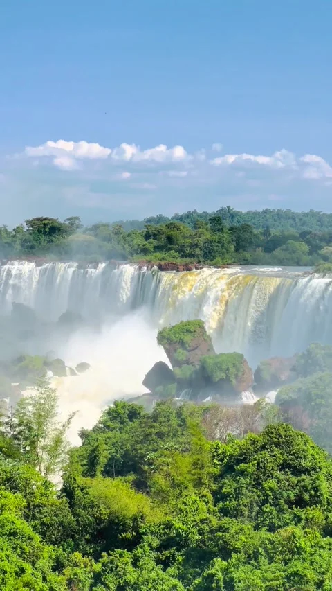 A scenic waterfall surrounded by lush greenery and mist on a sunny day. Stock Footage 276618062