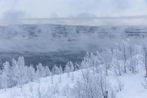 Scenic winter view of a steaming, ice-free bay surrounded by snow-covered hills Stock Photos