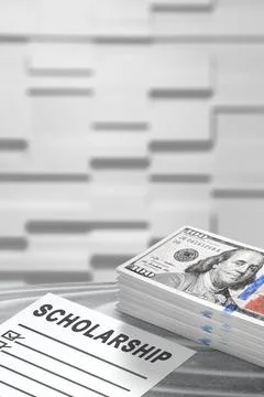 A scholarship application form placed next to a stack of one hundred dollar.. Stock Photos