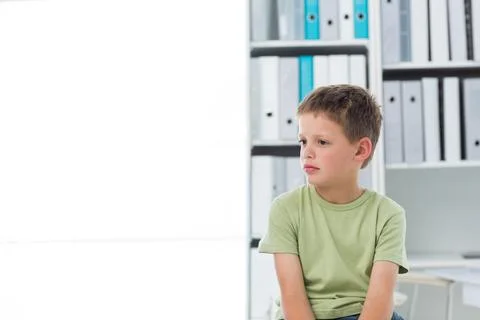 School-age boy sitting right in office near binder shelves, wearing light green Stock Photos