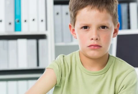 School-age boy sitting at study desk wearing green tee with white binders, Stock Photos