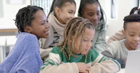 School age classmates leaning around laptop at classroom desk, screen lighting Stock Footage 341062698
