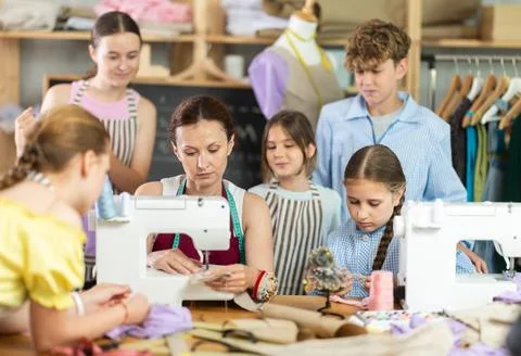 School-age students learning sewing from female instructor in tailoring workshop Stock Photos